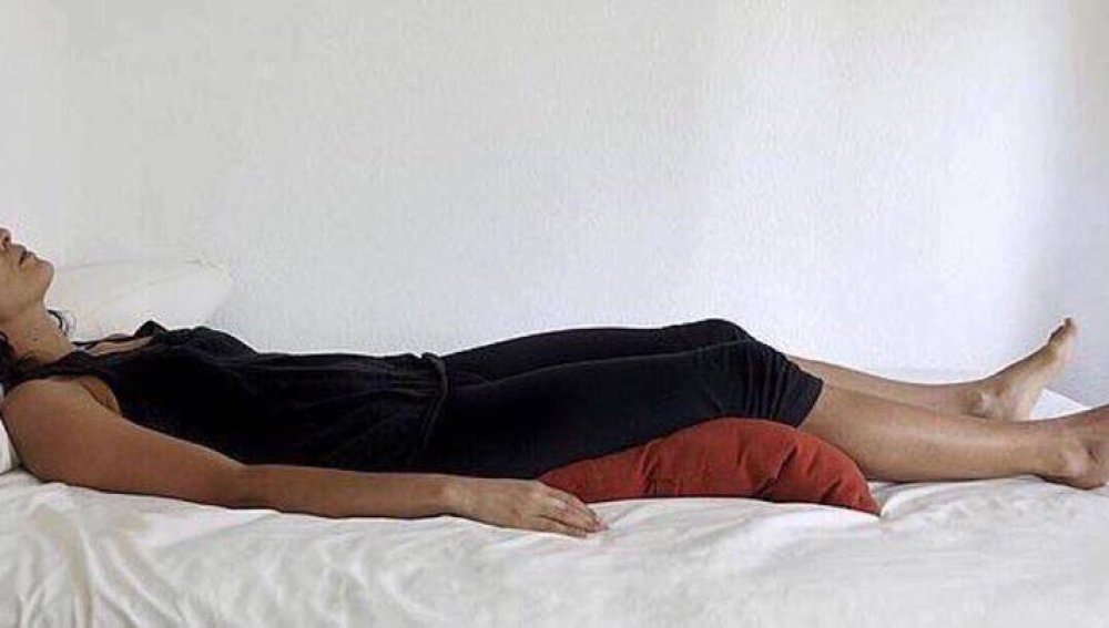 Imagen de mujer acostada con almohadas debajo de las rodillas 