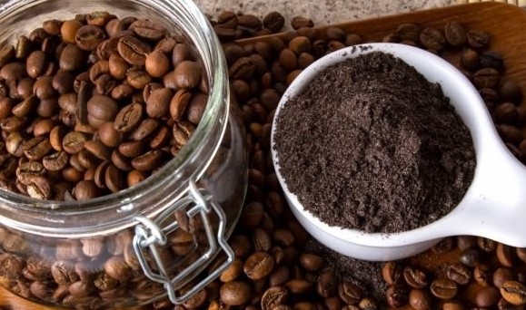 frasco de vidrio con semillas de café al lado de pequeño recipiente con café molido.
