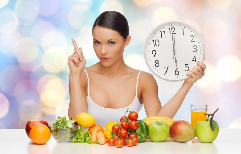 Mujer frente a mesa de frutas con reloj en la mano.