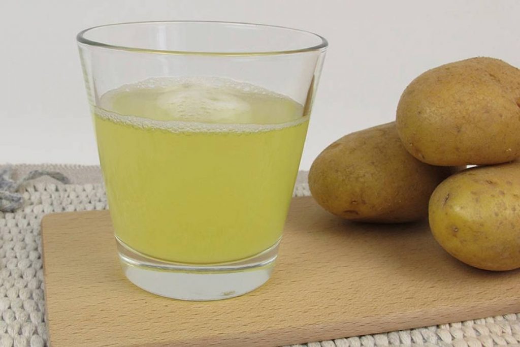 tres patatas y un vaso de jugo de patatas sobre una tabla en una mesa