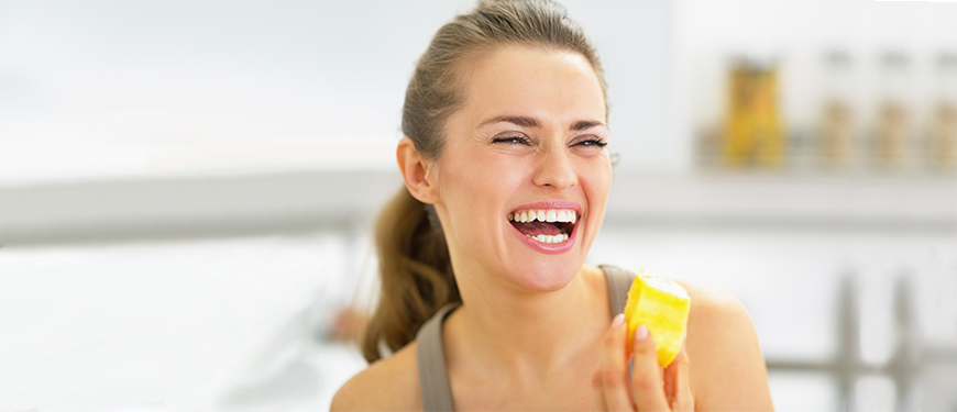 mujer sonriendo con un trozo de piña en la mano.