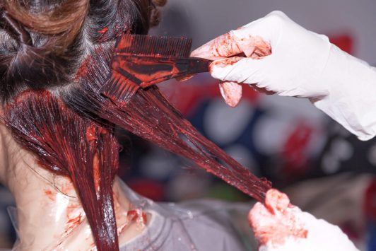 Primer plano de mujer colocándose tinte natural de zanahoria y remolacha en el cabello.